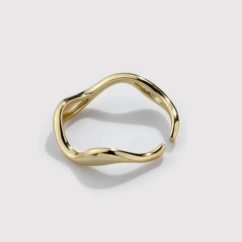 Gold ring with a wavy design on a light gray background
