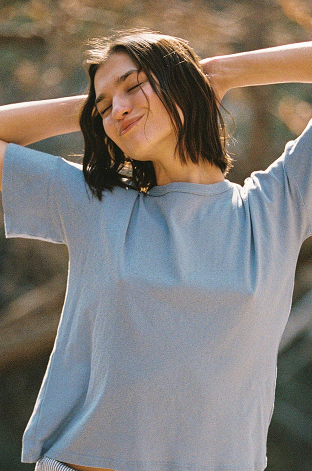 Woman in a light blue t-shirt with arms outstretched outdoors