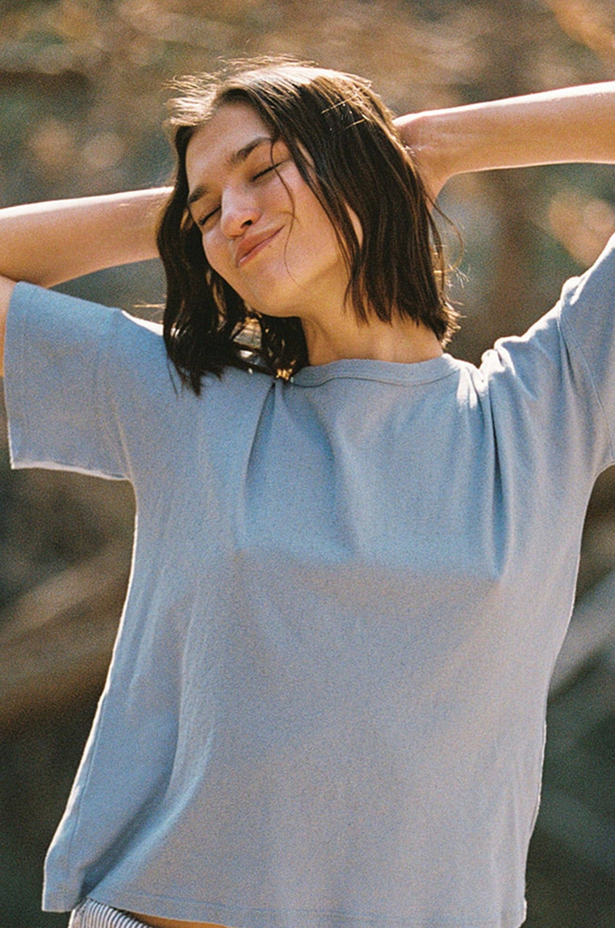 Woman in a light blue t-shirt with arms outstretched outdoors
