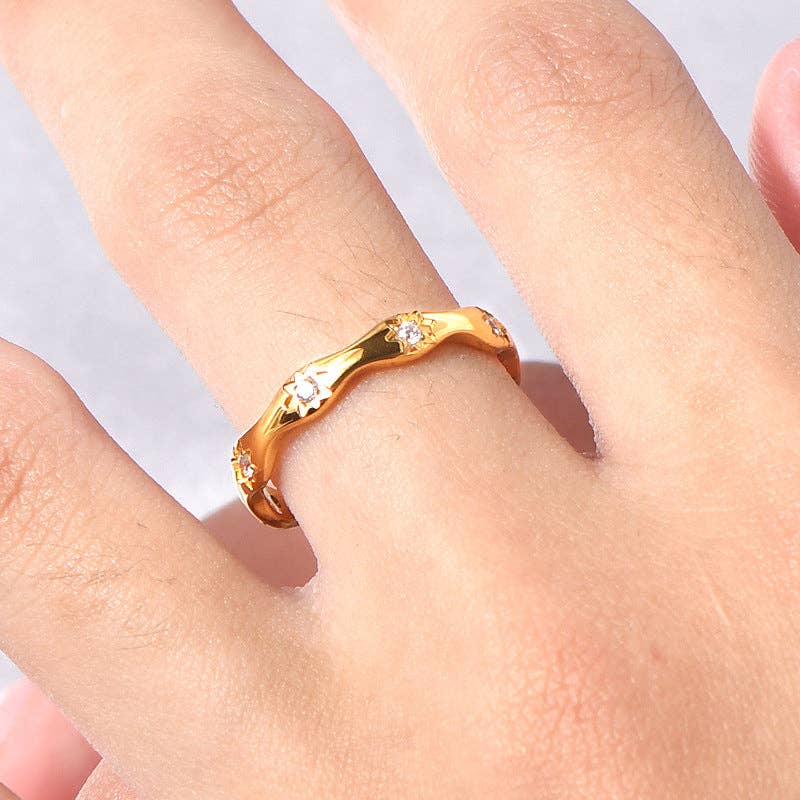 Gold ring with small diamonds on a finger against a light background