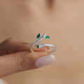 Silver ring with green gemstones shaped like leaves on a blurred background